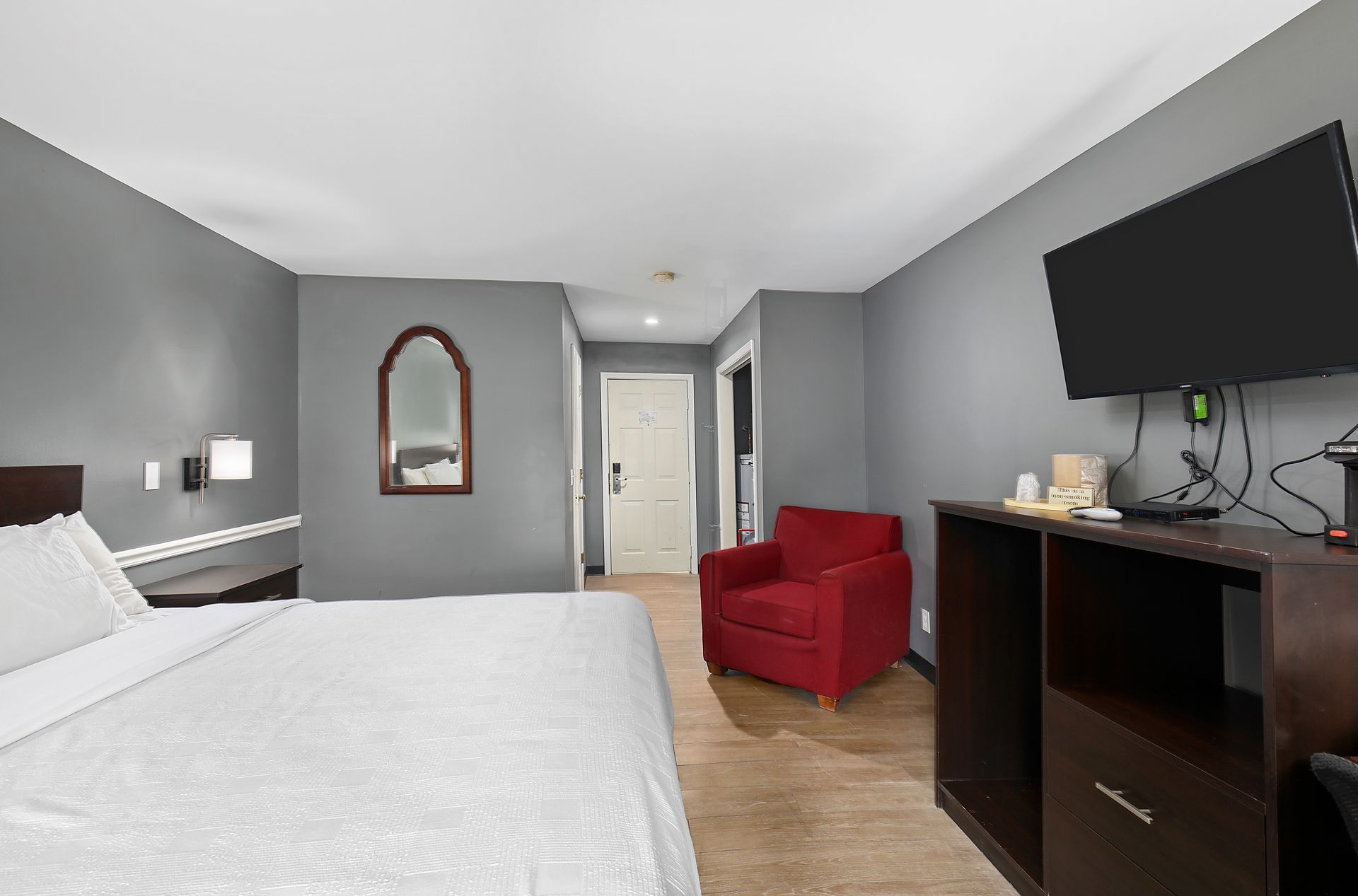 A hotel room with a king size bed , chair , desk and television.