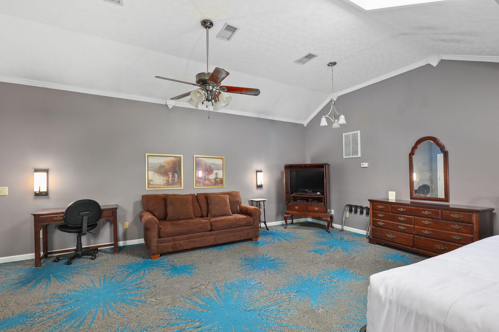 A hotel room with a couch , dresser , desk and television.