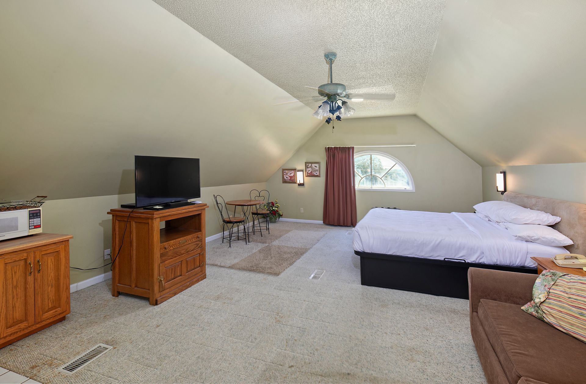 A bedroom with a bed , couch , television and a ceiling fan.