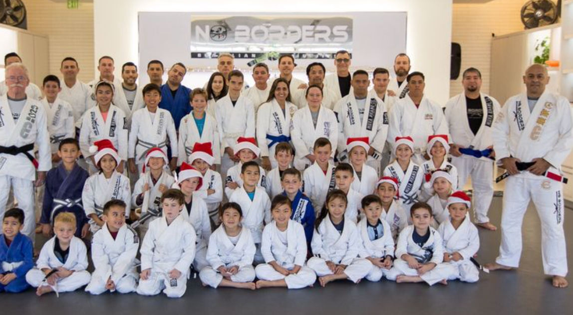 Group of people in martial arts uniforms, some with Santa hats, posing for a group photo in a gym.