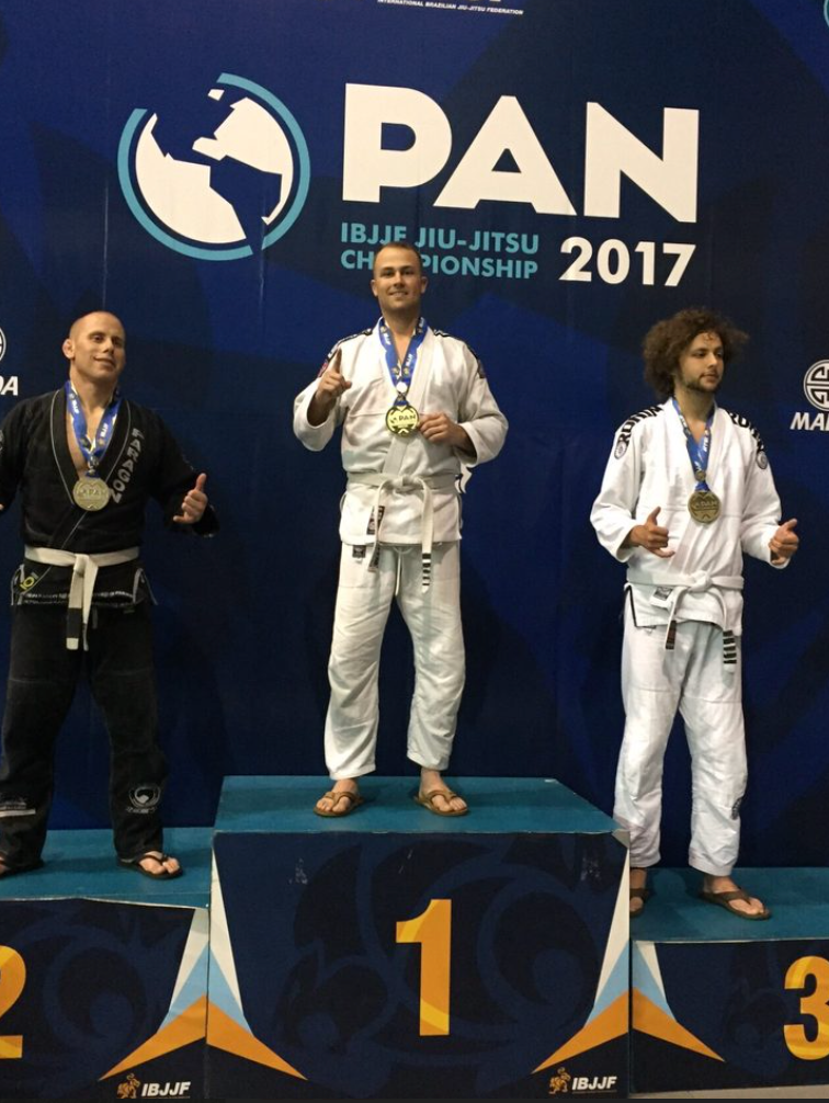 Podium at IBJJF Jiu-Jitsu Championship 2017. Gold medalist in white gi with thumbs up, flanked by silver and bronze medalists.