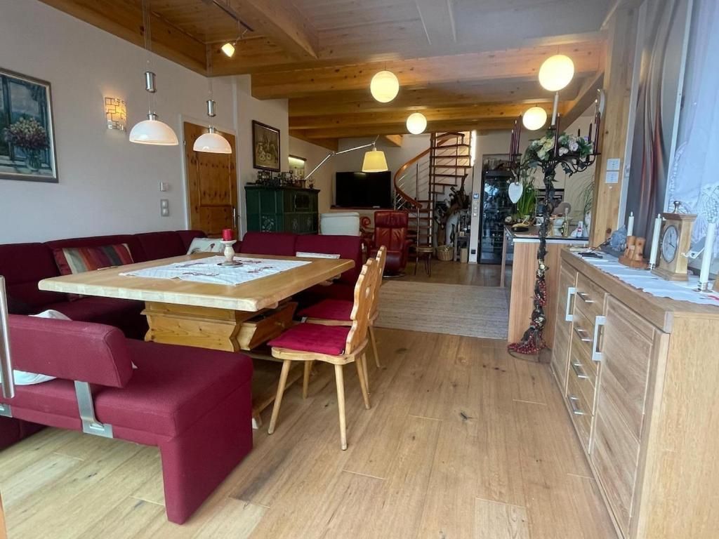 Gemütliches Esszimmer mit roten Stühlen, Holztischen, warmem Licht und einer Treppe im Hintergrund