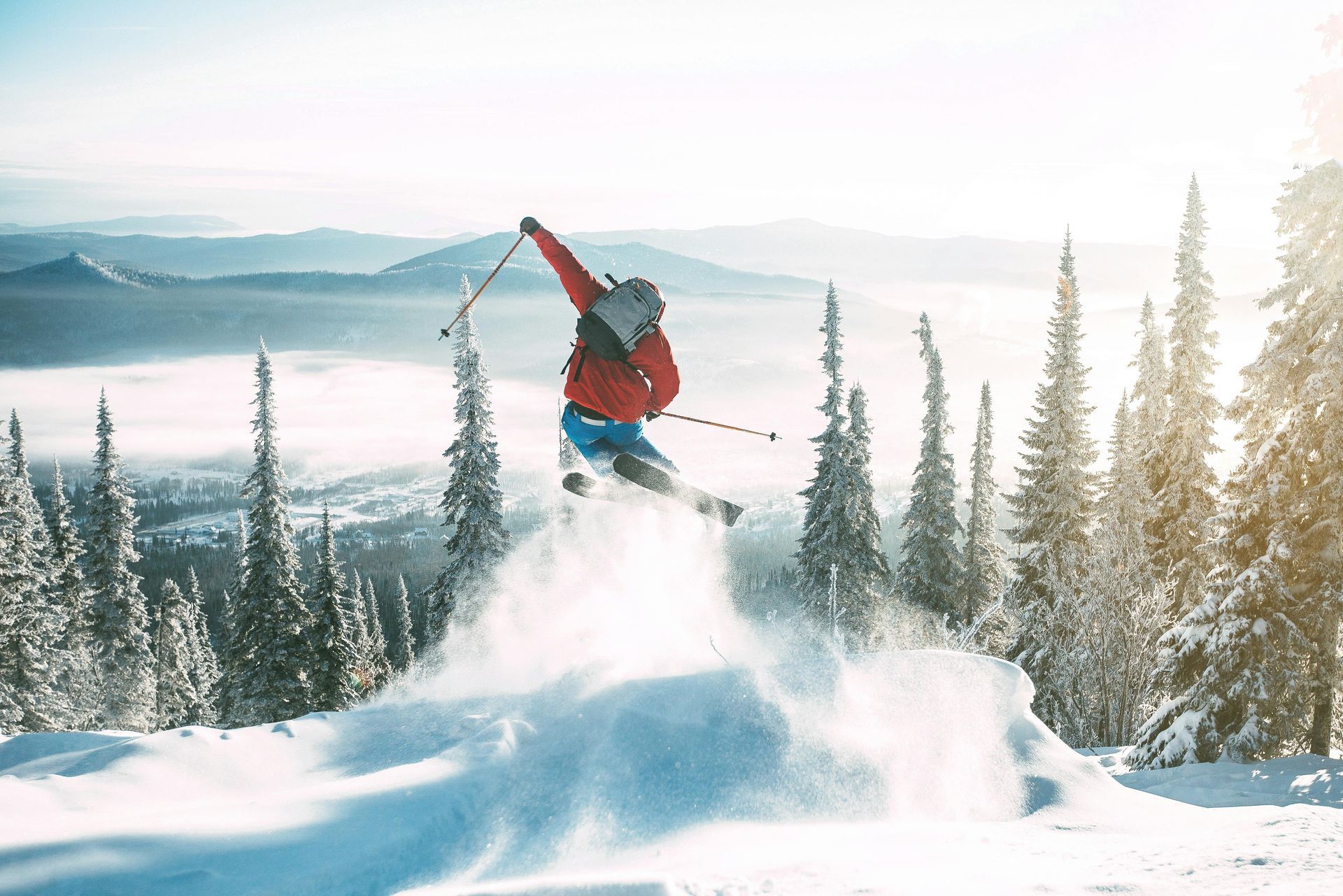 Ein Skifahrer in einer leuchtend roten Jacke springt von einem schneebedeckten Bergrücken