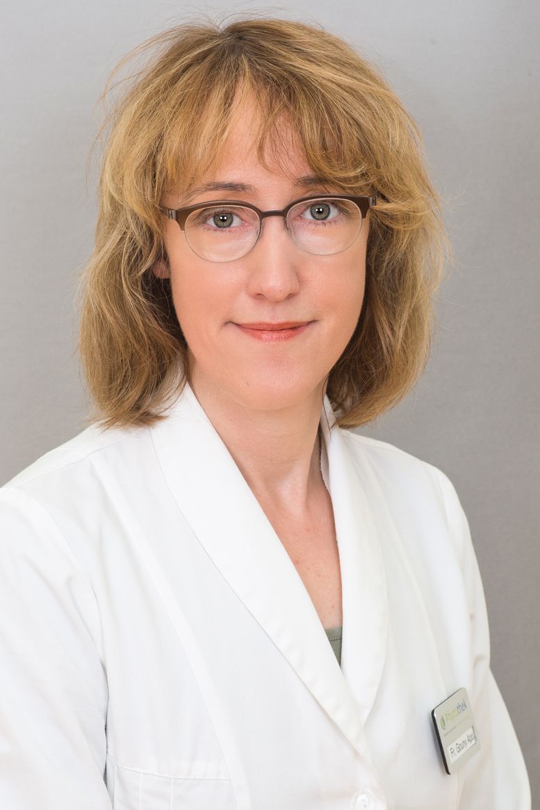 Eine Frau mit Brille und weißem Laborkittel lächelt in die Kamera.