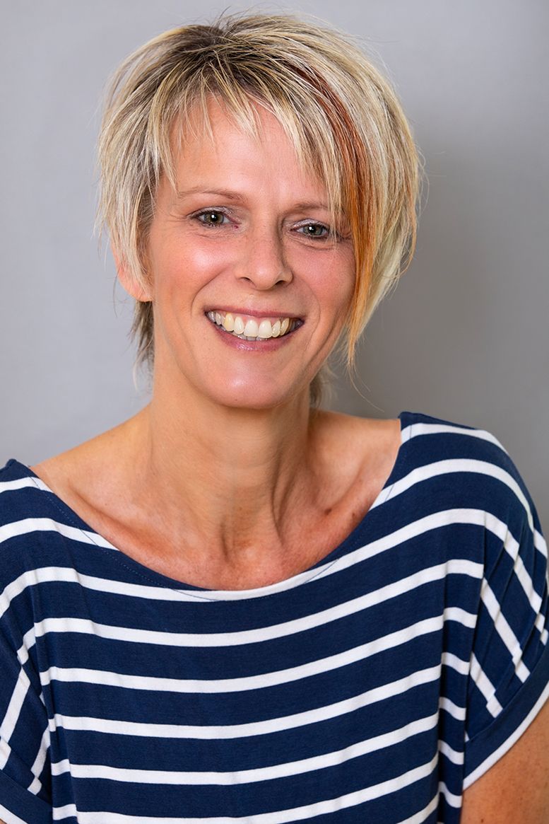 Eine Frau in einem blau-weiß gestreiften Hemd lächelt in die Kamera.