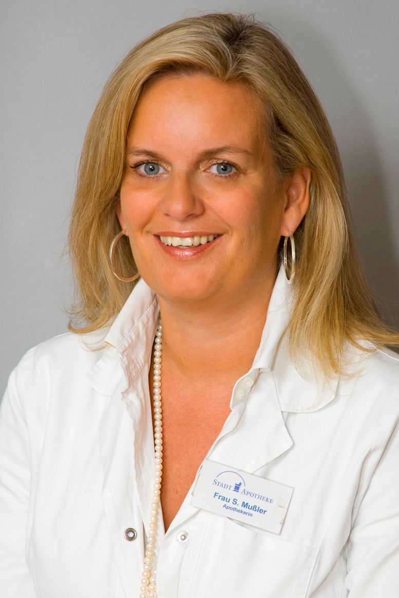 Eine Frau in einem weißen Laborkittel lächelt in die Kamera.