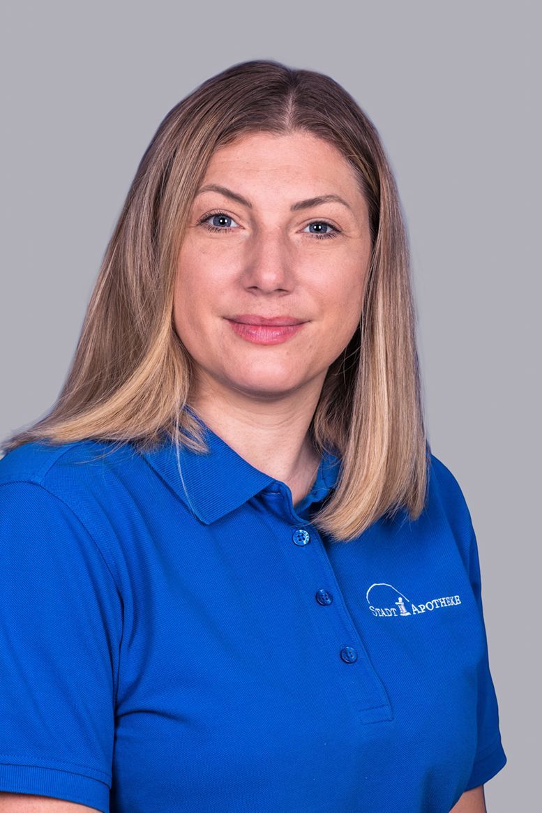 Eine Frau in einem blauen Poloshirt lächelt in die Kamera.