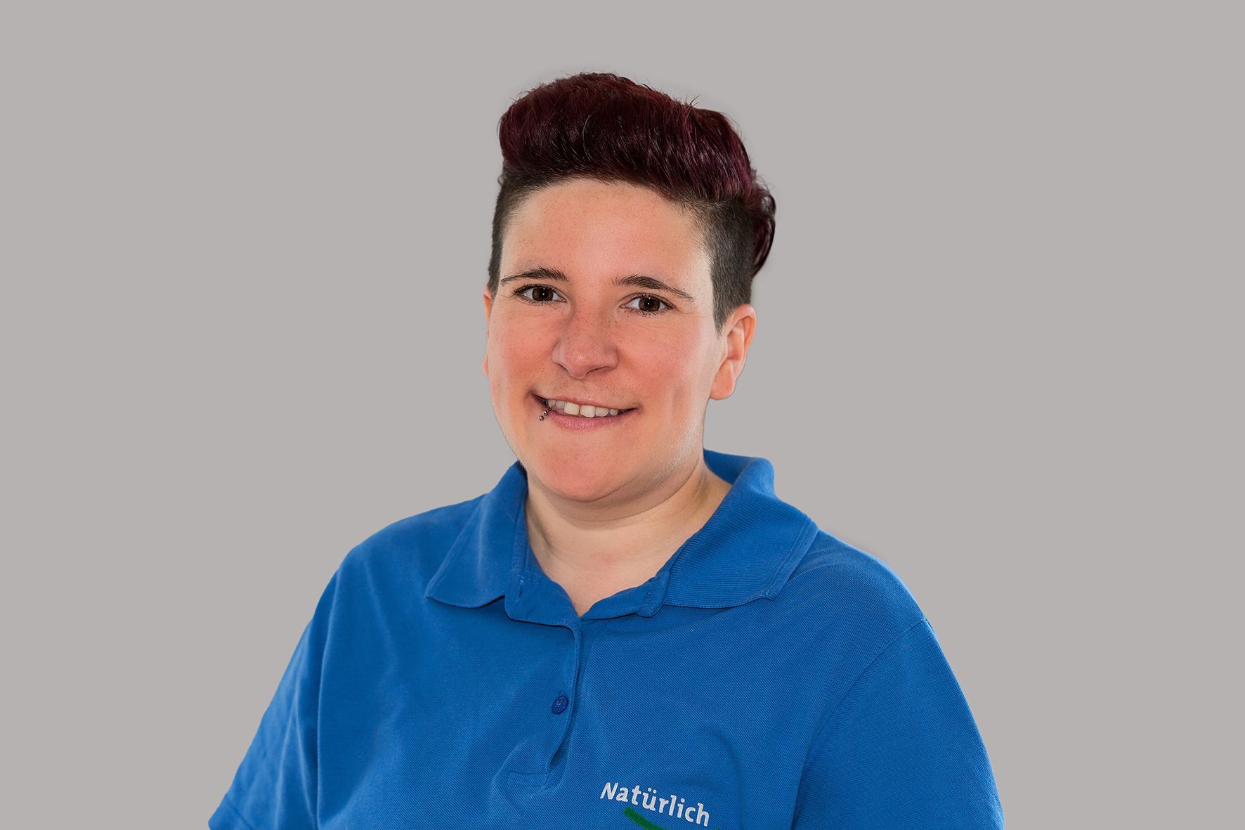 Eine Frau trägt ein blaues Poloshirt und lächelt.