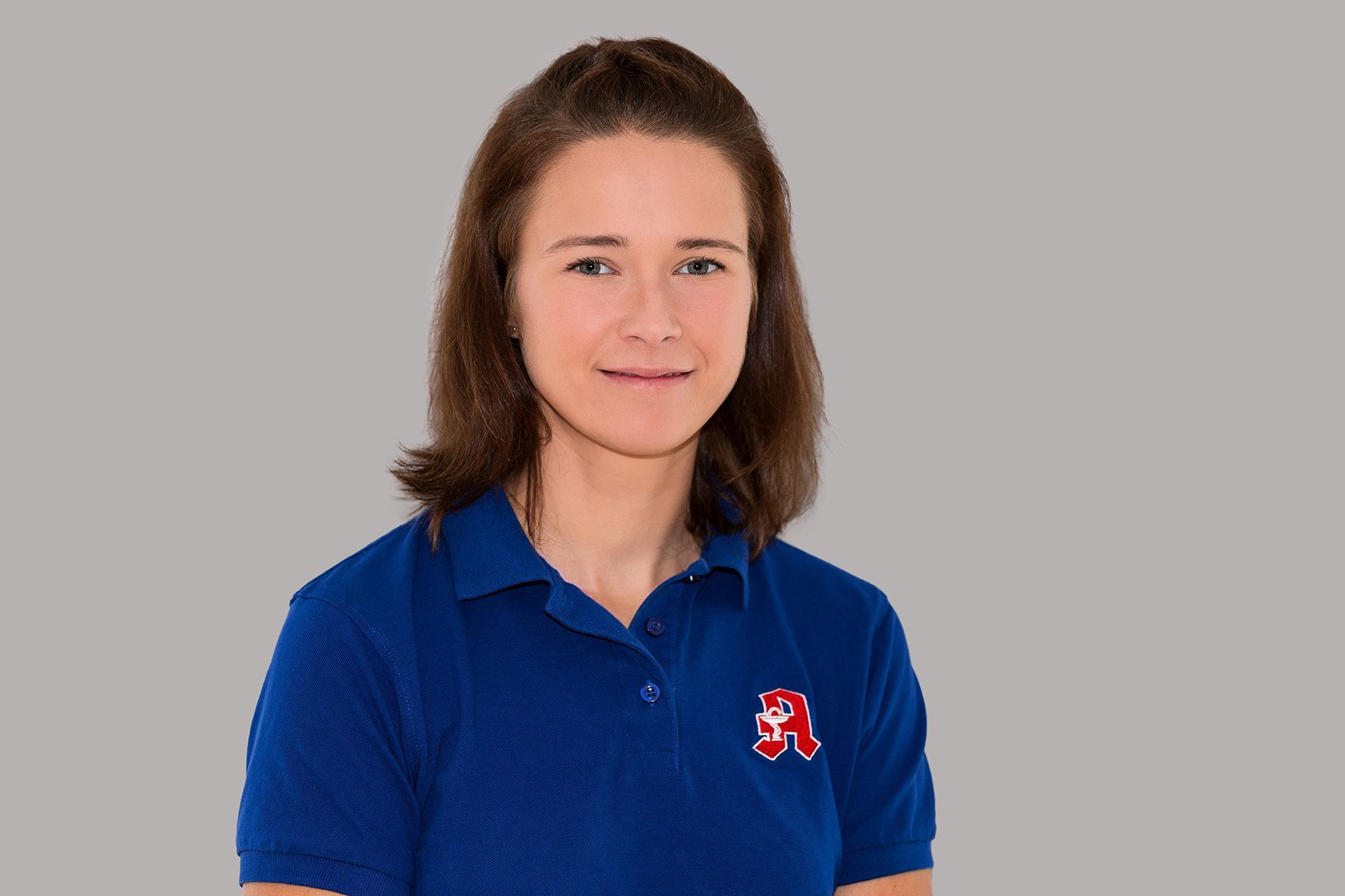 Eine Frau in einem blauen Poloshirt steht vor einem grauen Hintergrund.