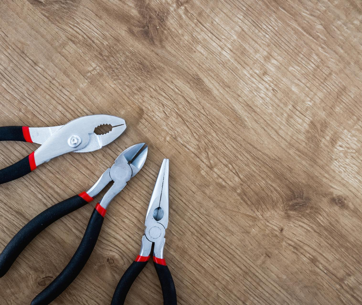 Three pliers with black handles and red accents on a wood surface.
