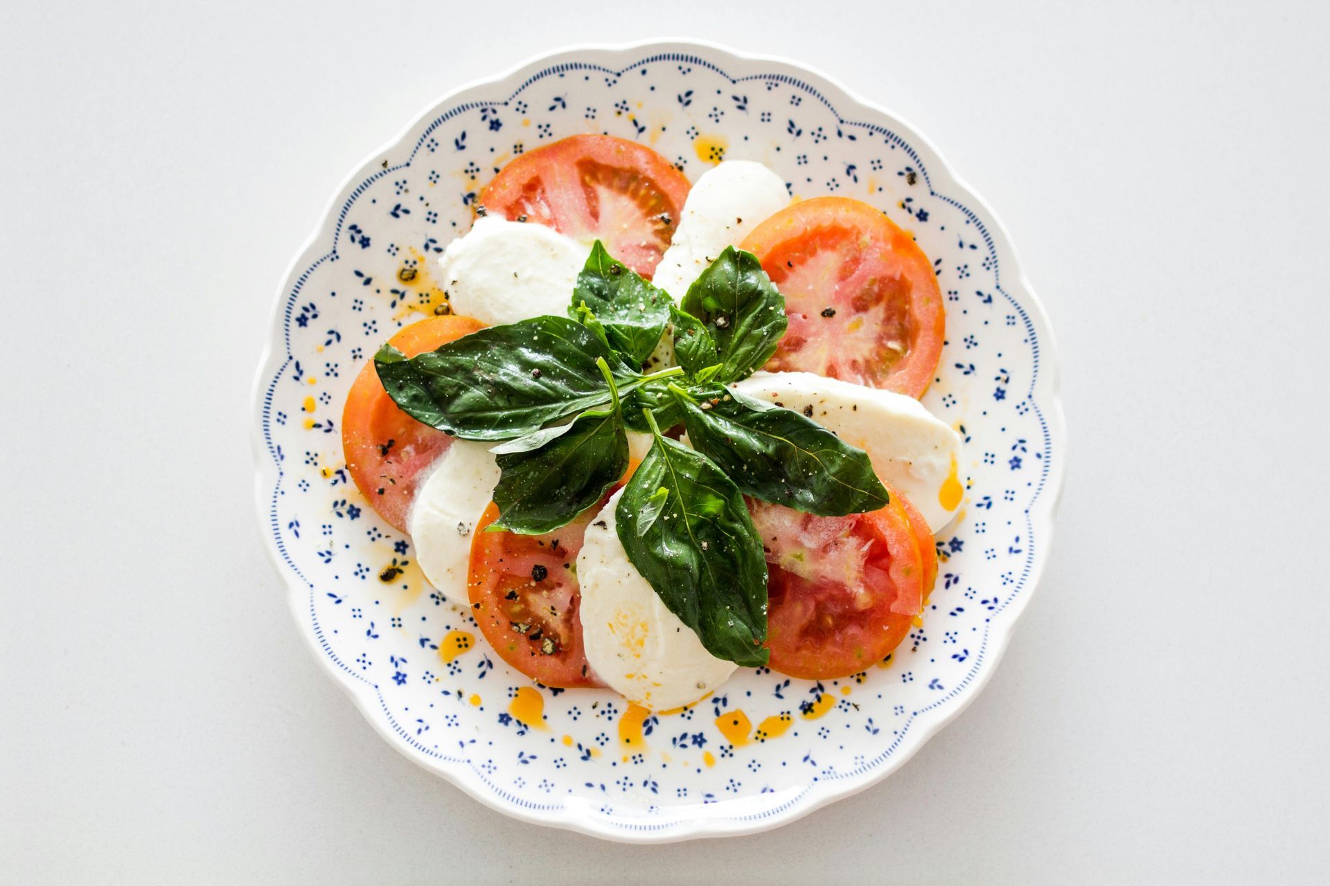 Caprese salad with tomato, mozzarella, basil, on a floral plate.