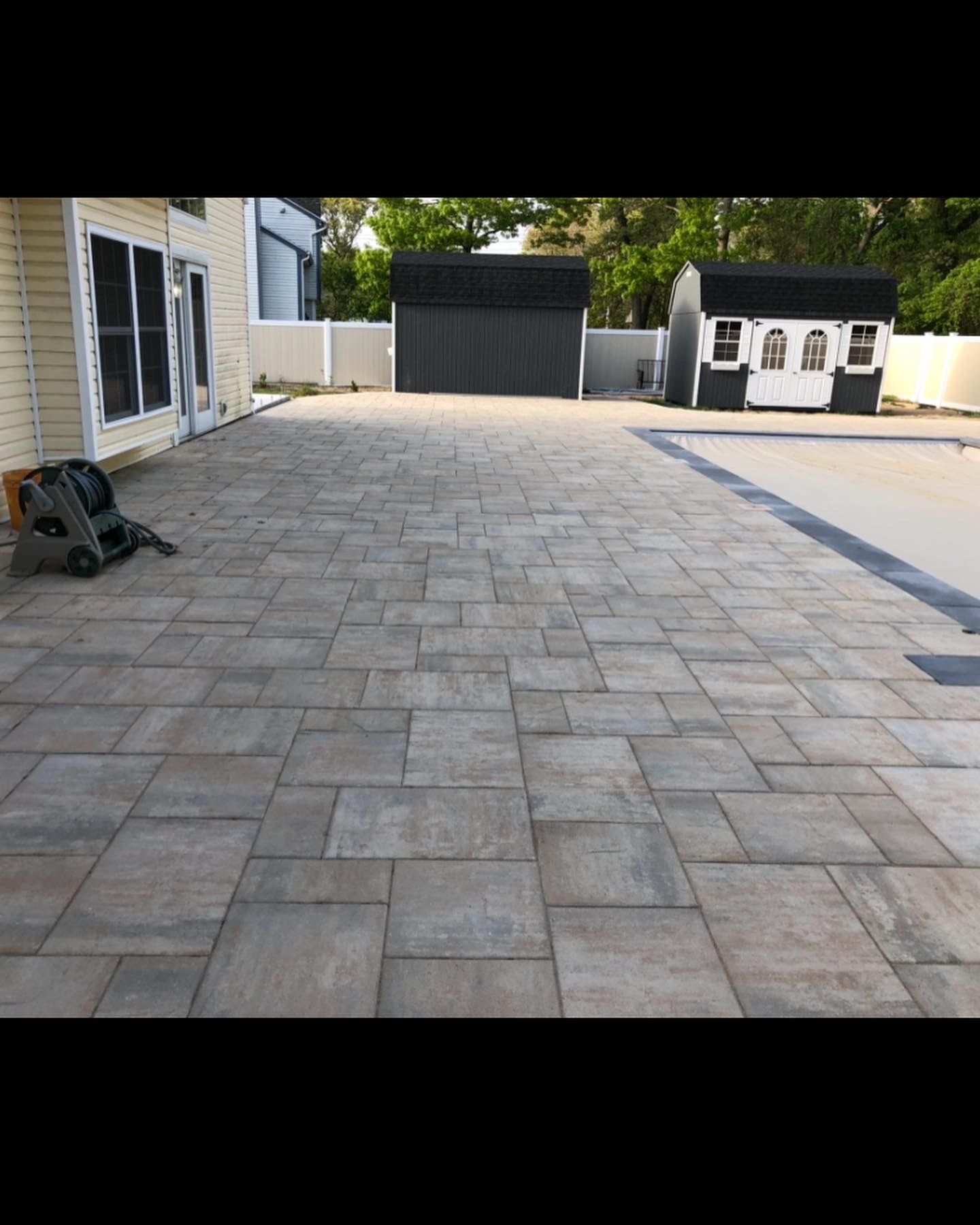A patio with a shed and a garage in the background.