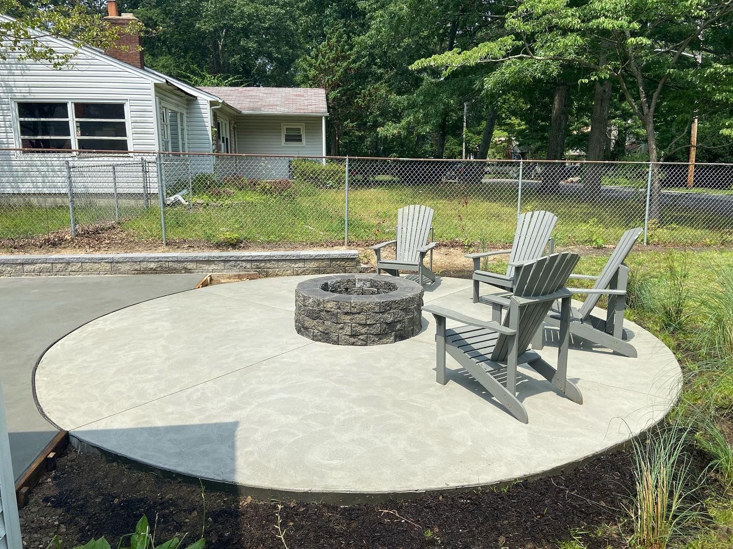 A circular patio with a fire pit and chairs in front of a house.
