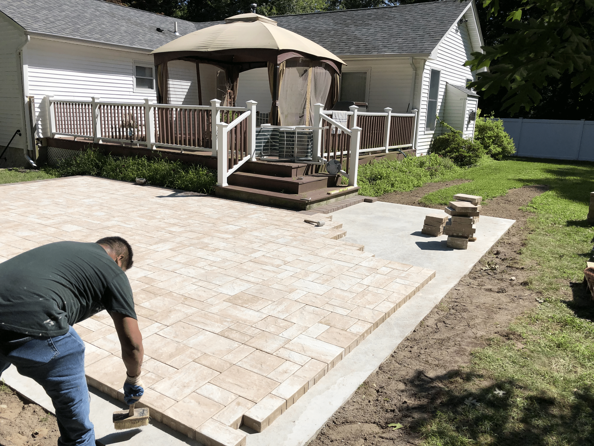 A man is laying bricks on a patio in front of a gazebo.