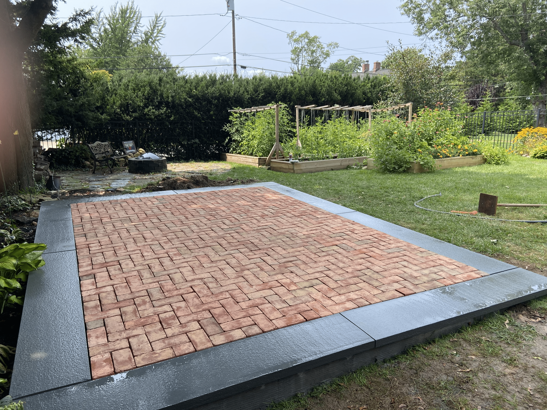 A brick patio in a backyard with a garden in the background.