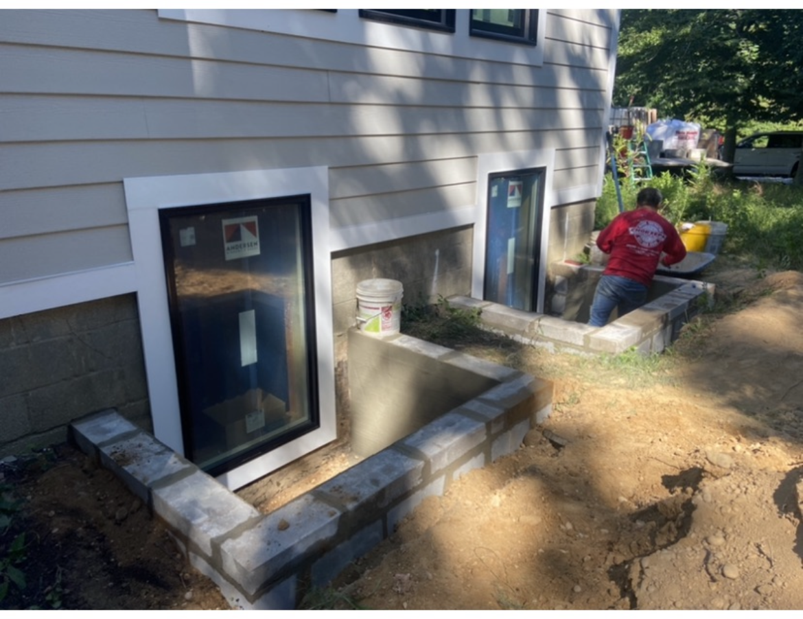 A man in a red shirt is standing in front of a house.