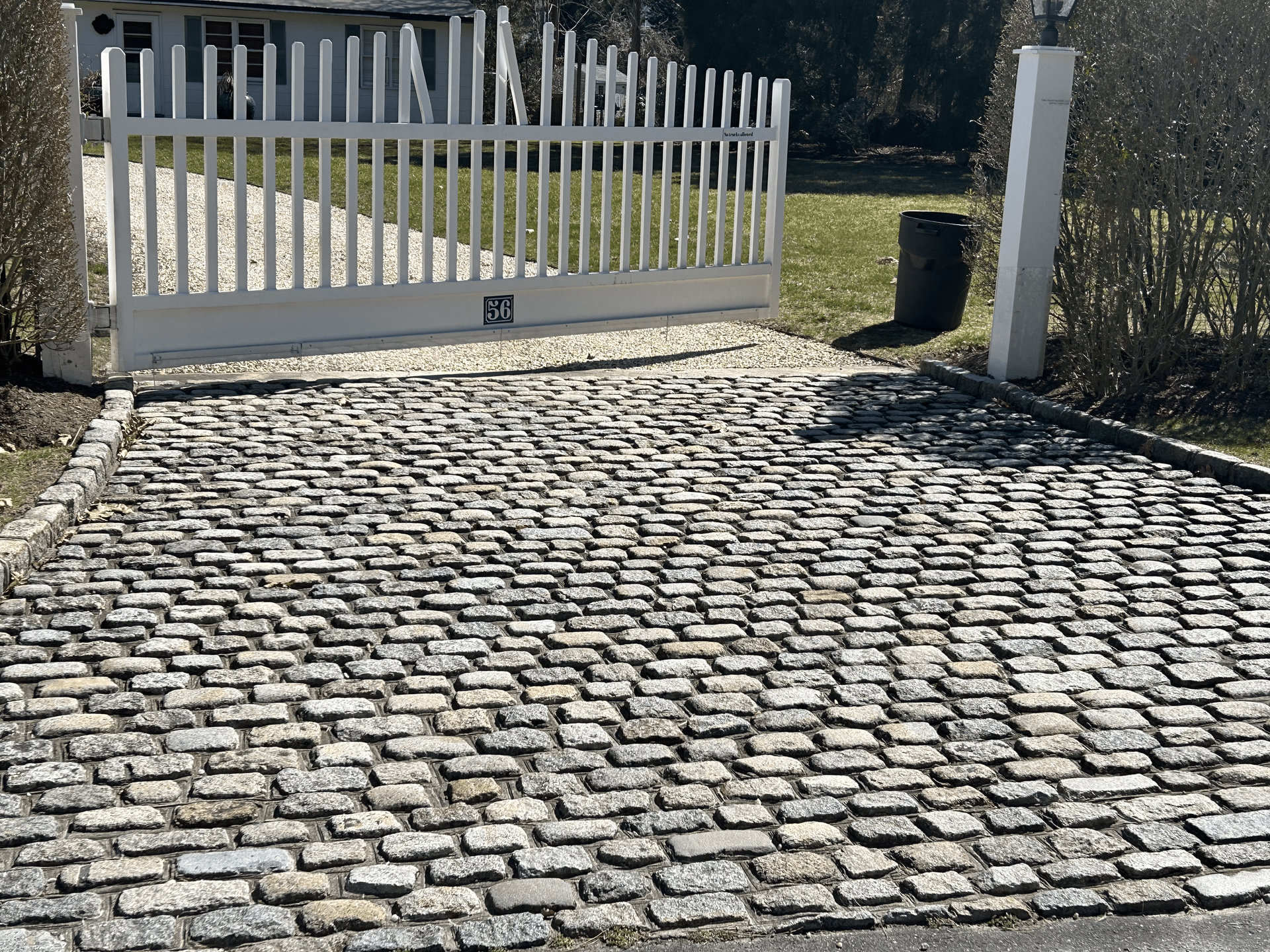 A brick driveway with a white fence in the background.