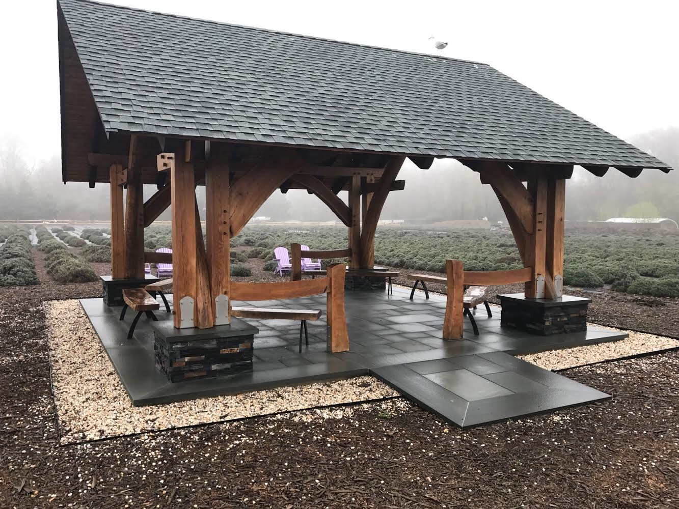 A wooden pavilion with a roof and benches in a field.
