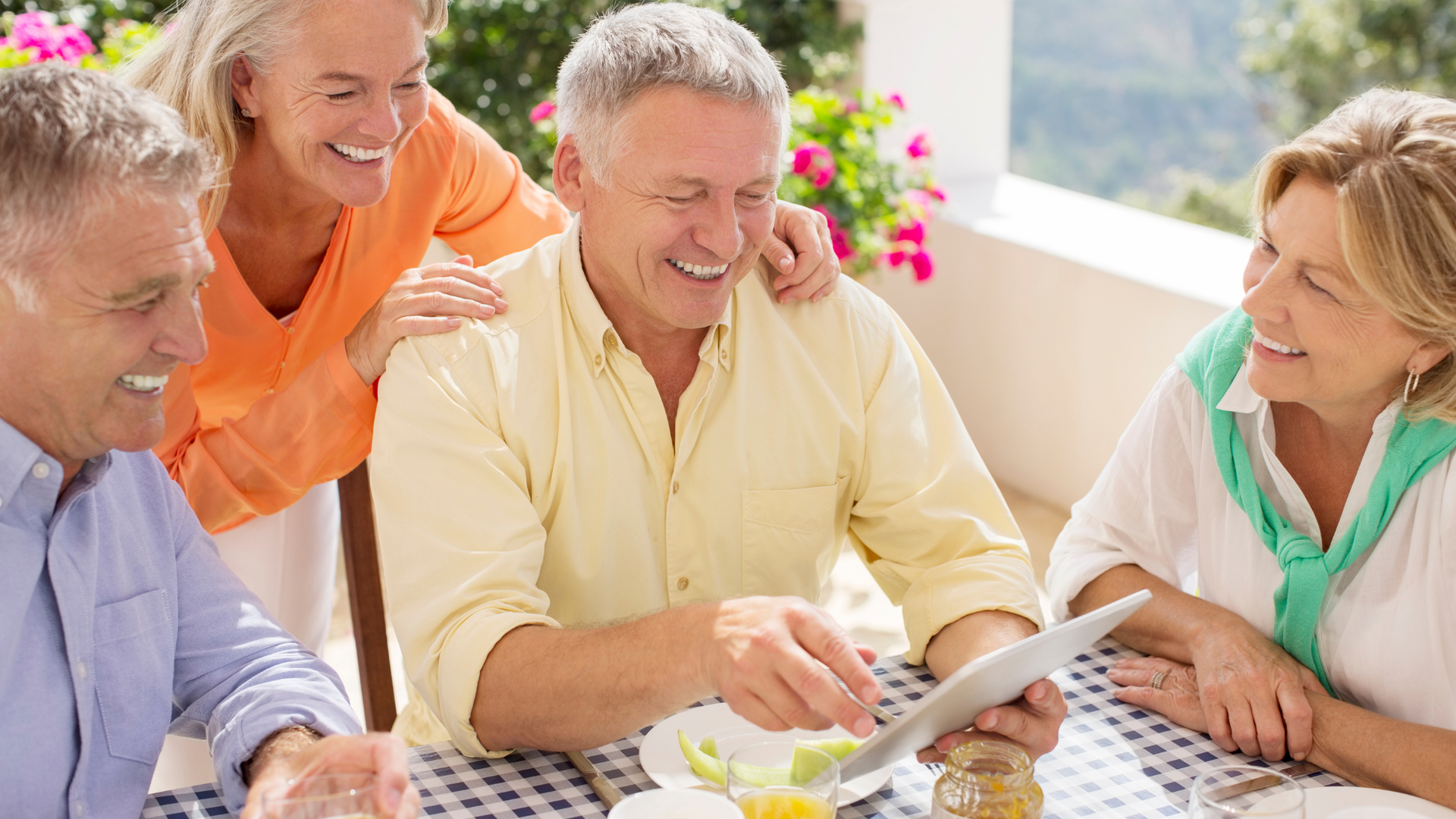 A group of older people are sitting at a table looking at a tablet.
