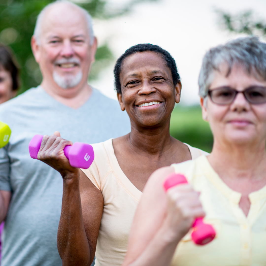 A group of people are holding pink dumbbells and smiling.