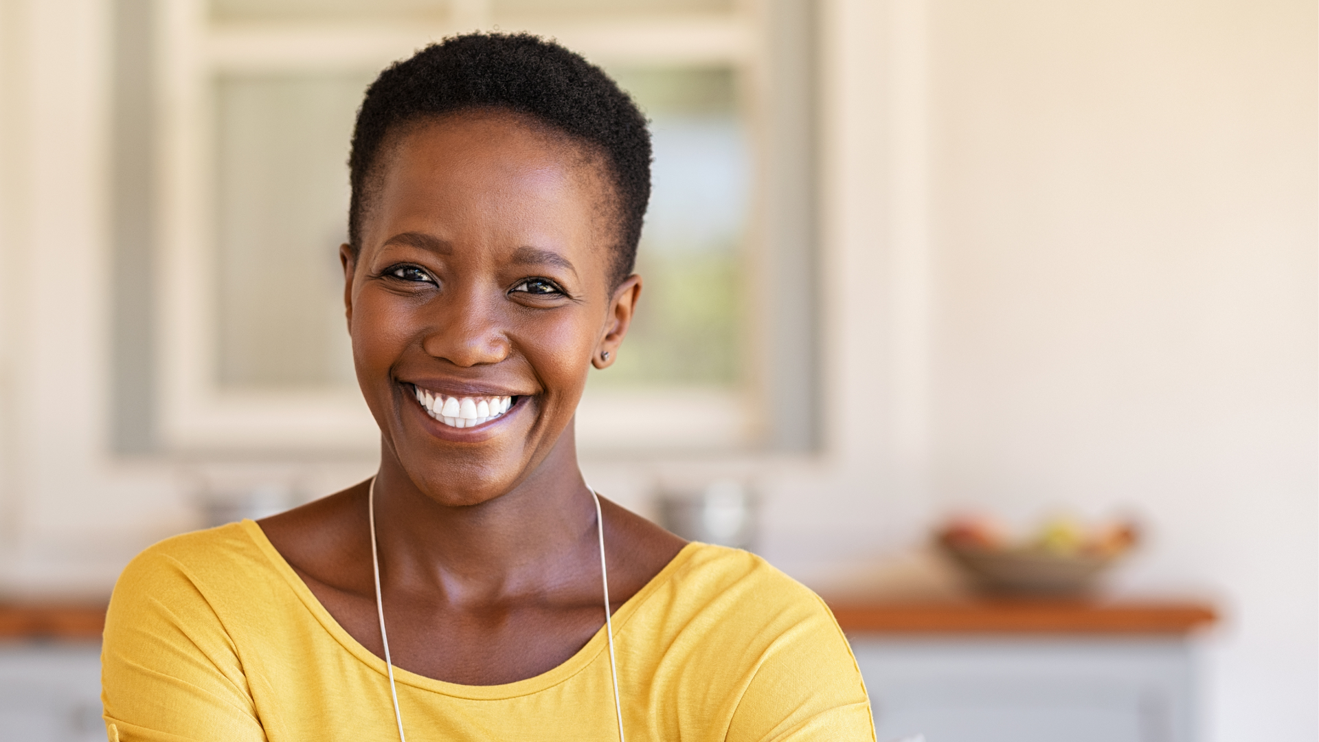 A woman in a yellow shirt is smiling for the camera in a kitchen.