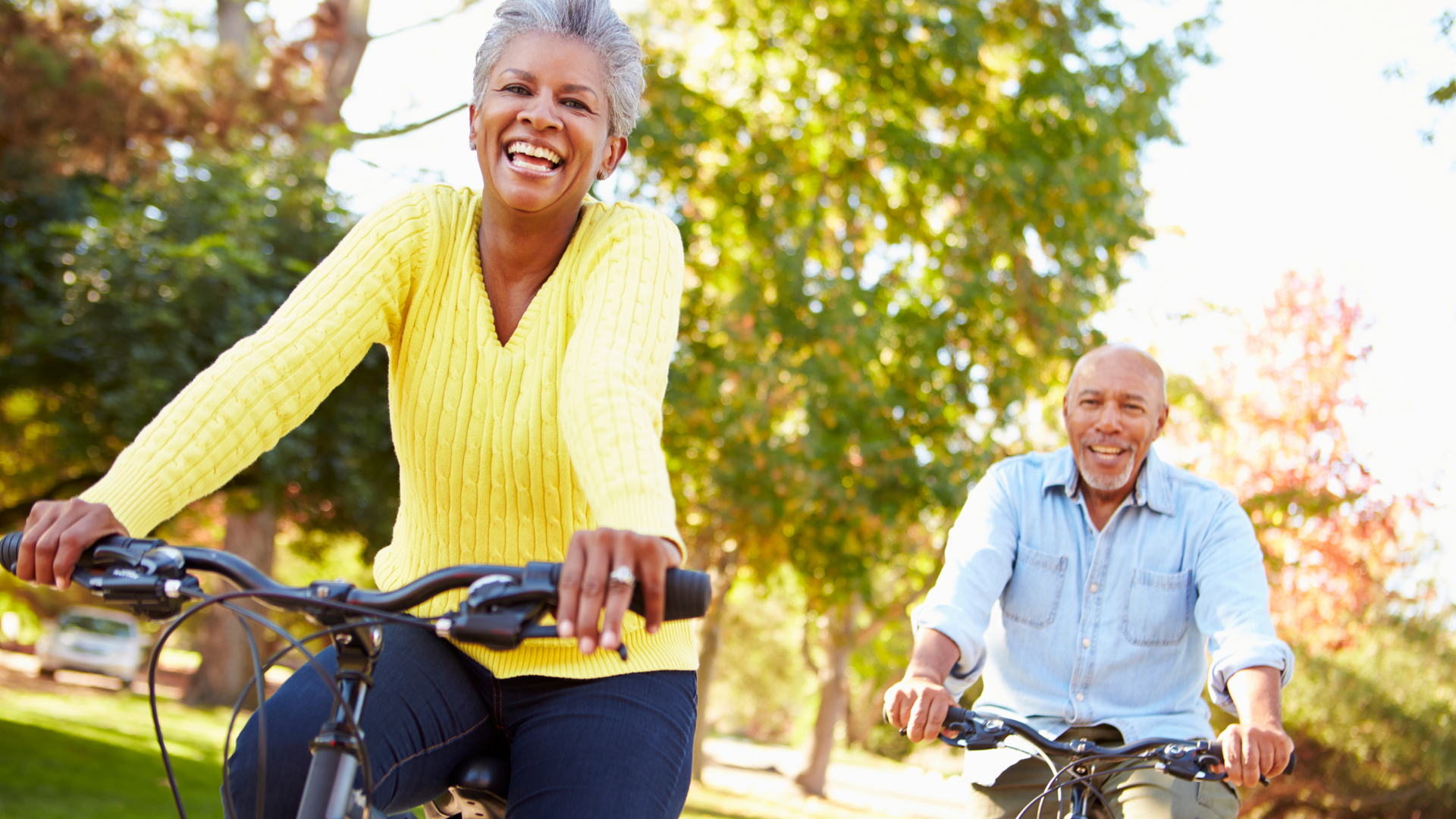 A man and a woman are riding bicycles in a park.