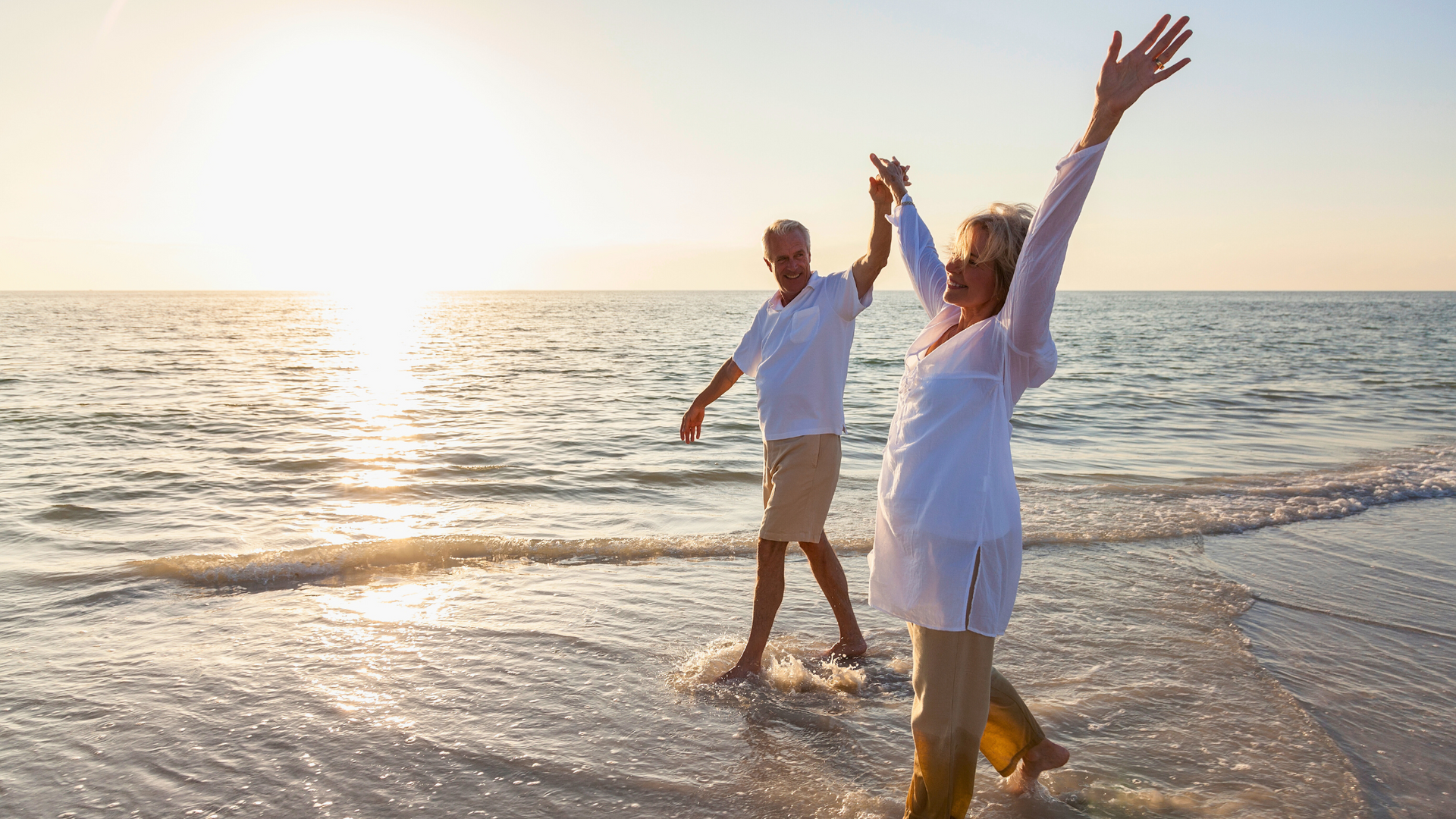 Older couple is dancing on the beach at sunset.