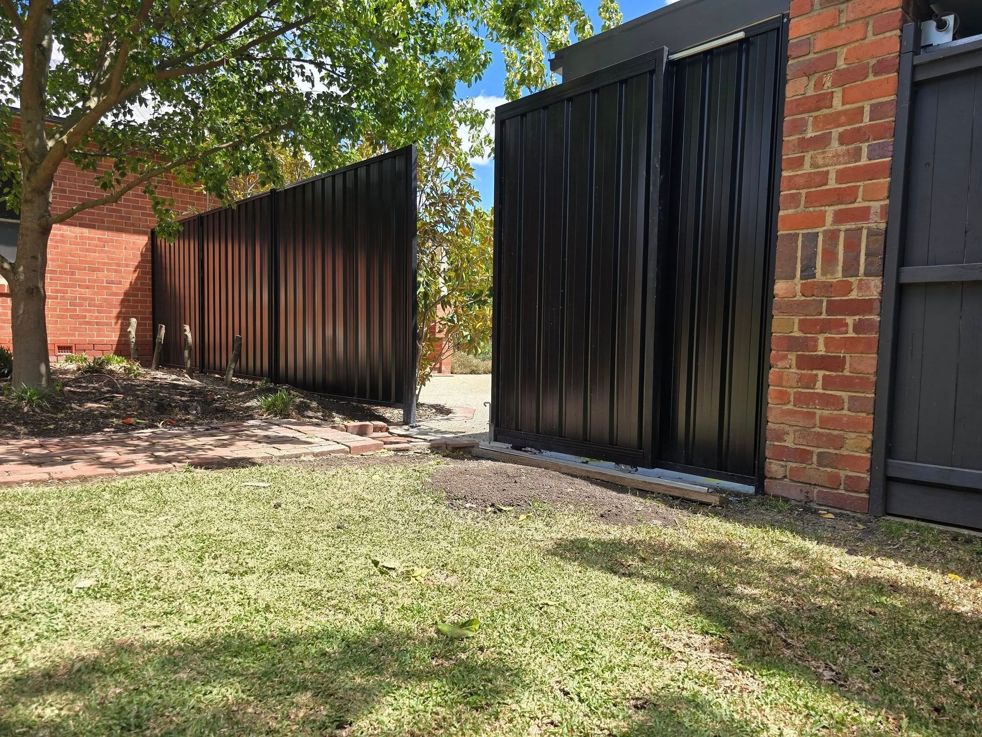 Black metal gate and fence in front of a brick building on green grass.