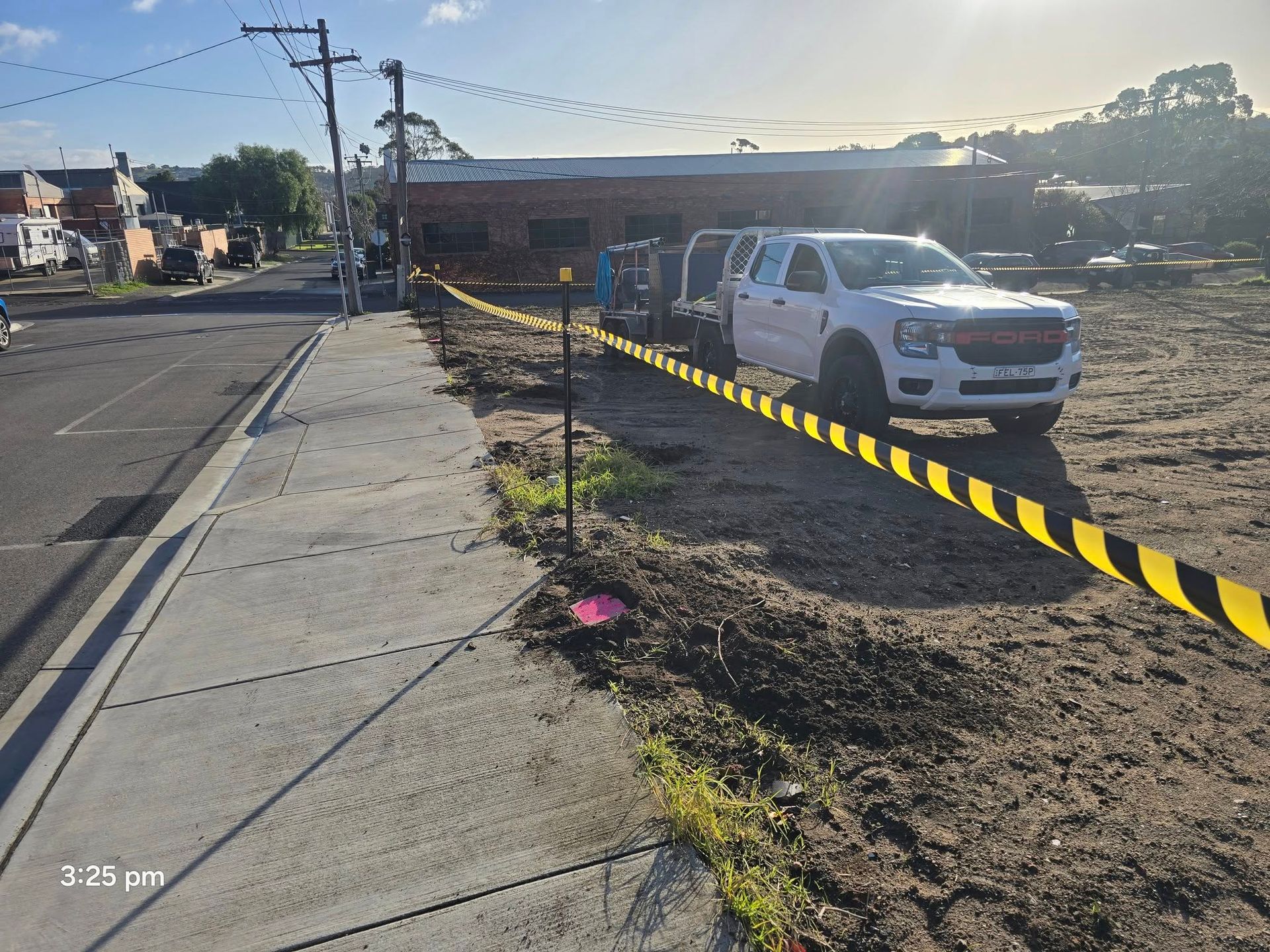A white truck parked next to a construction site. Yellow caution tape marks the perimeter along a sidewalk.