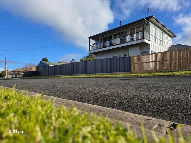 House behind a black fence, on a street with green grass and a blue sky.