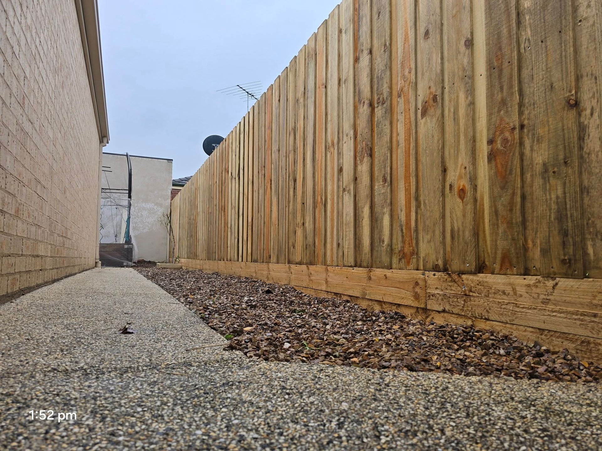 Gravel path next to a wooden fence and brick wall. Overcast sky.