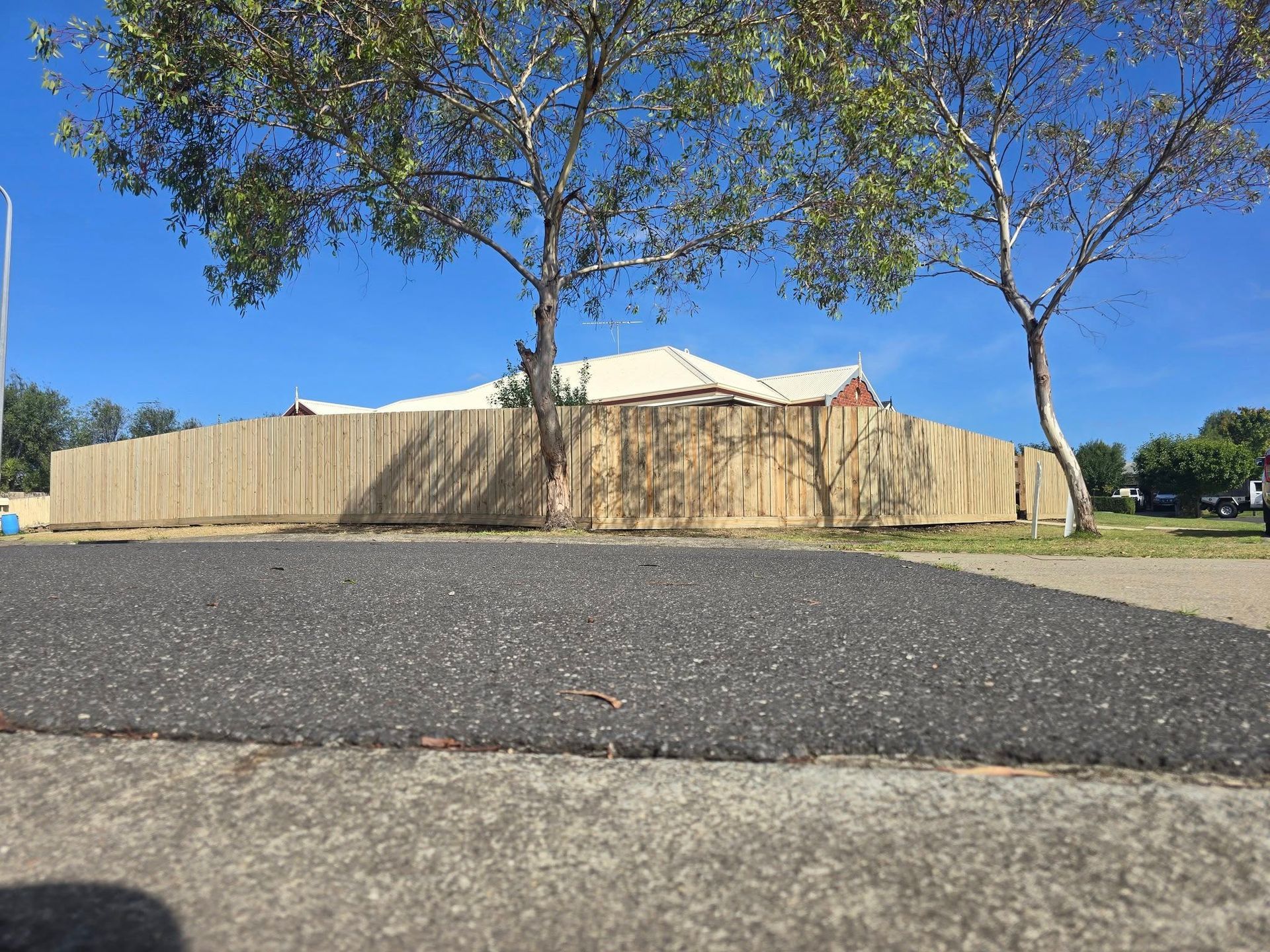 Wooden fence surrounding a house under a bright blue sky with two trees in front.
