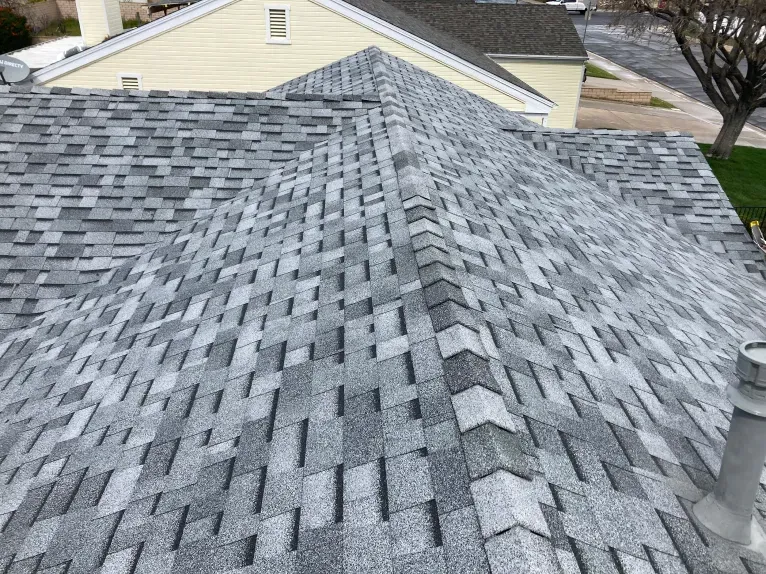 A roof with a lot of shingles on it and a yellow house in the background.
