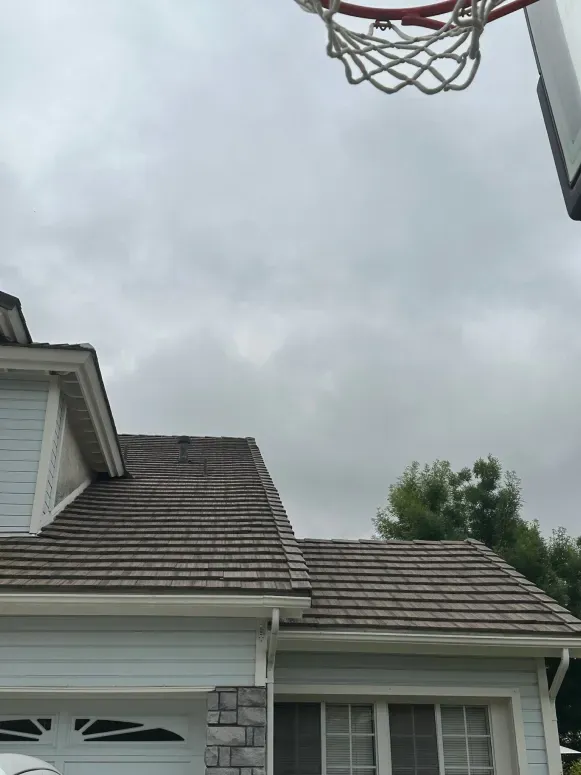 A basketball hoop is hanging from the roof of a house