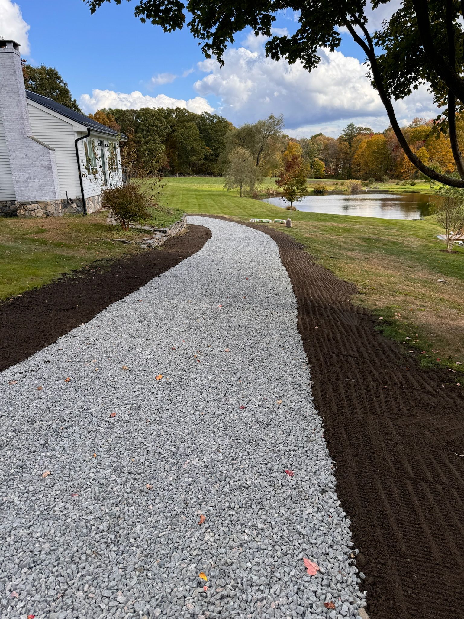 A gravel driveway leading to a house with a pond in the background.