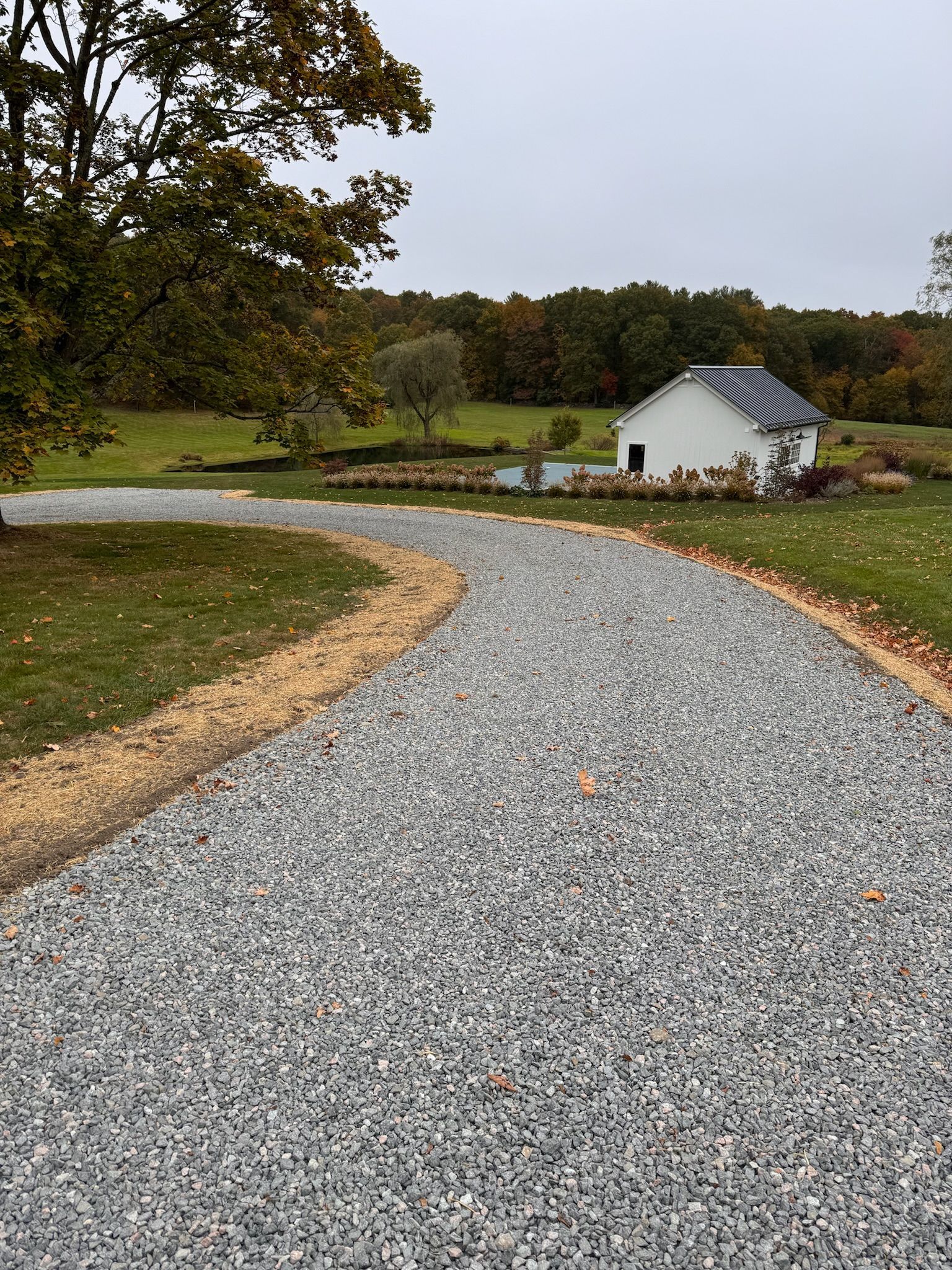 A gravel driveway leading to a white house in the middle of a field.