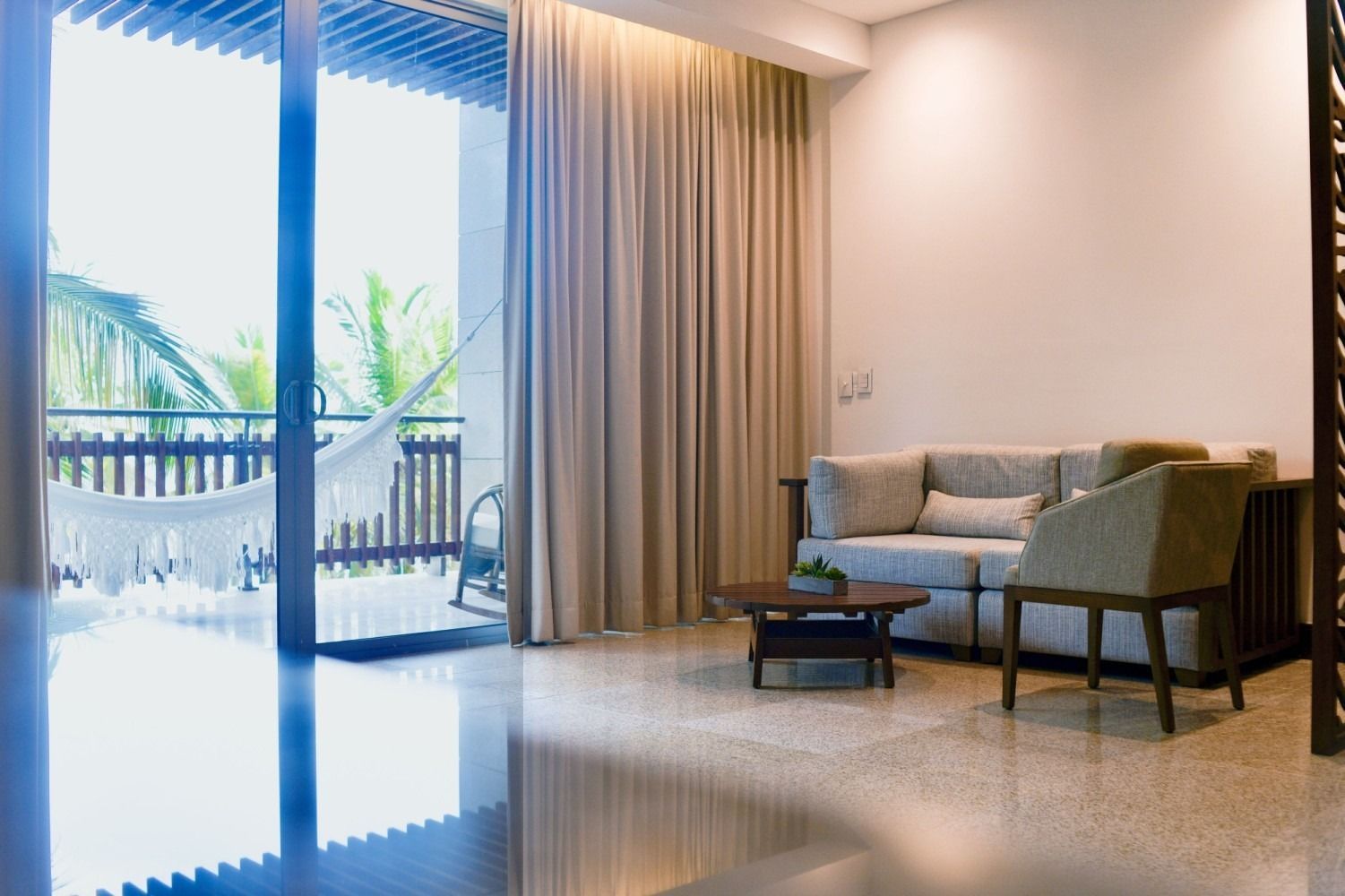 Living room with balcony view; light-colored curtains, sofa, chair, coffee table. 