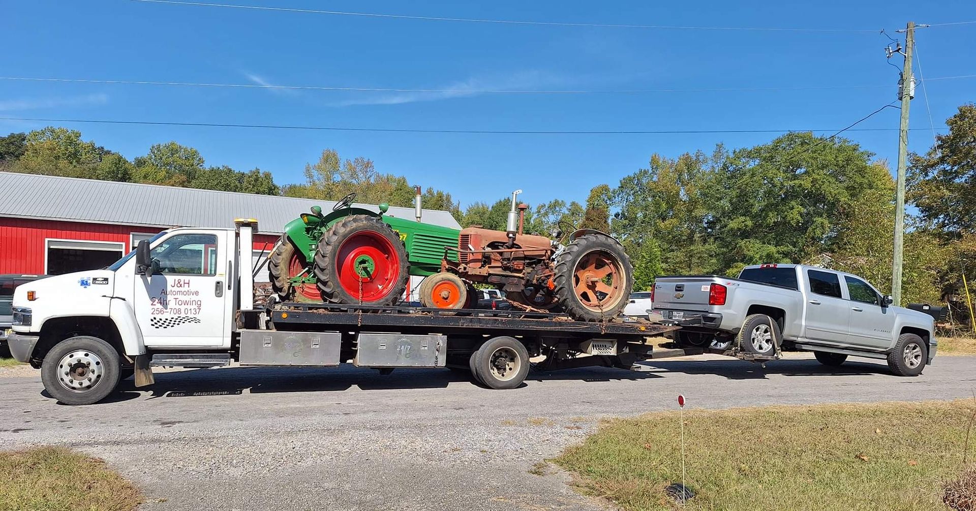 A tow truck is carrying a tractor on the back of it.