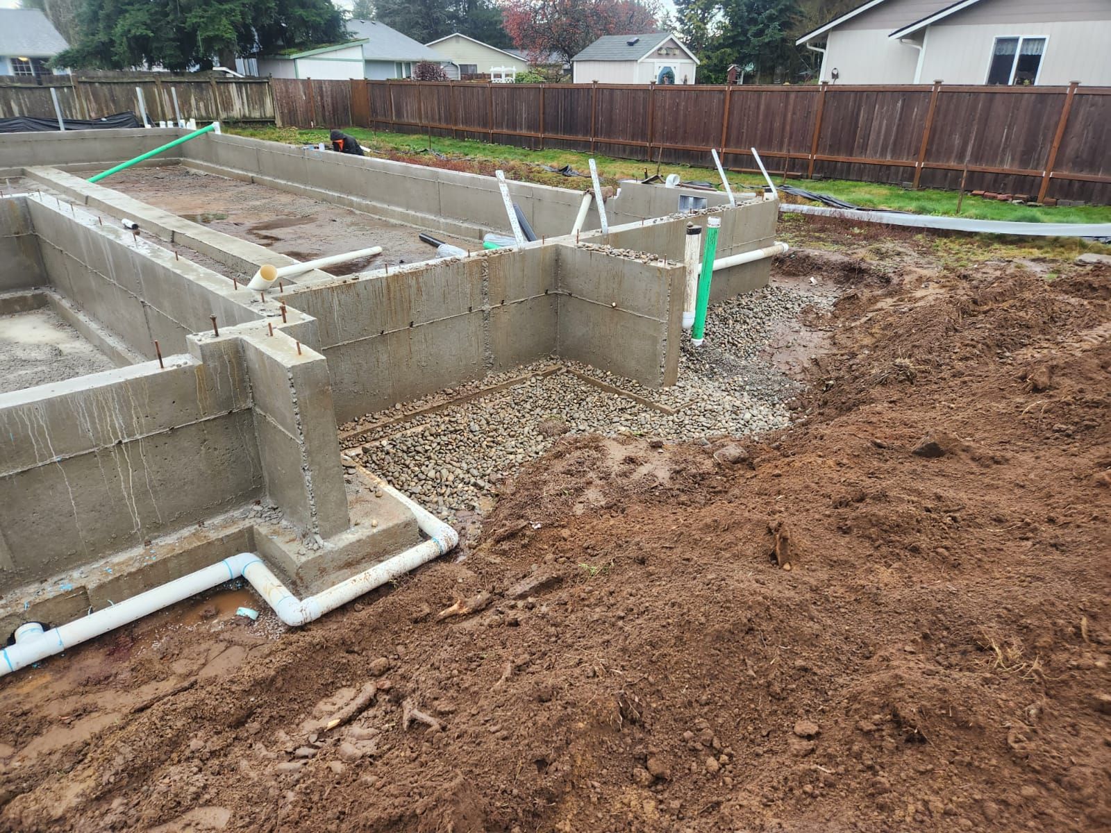 Concrete foundation for a building under construction, with exposed gravel and muddy ground.