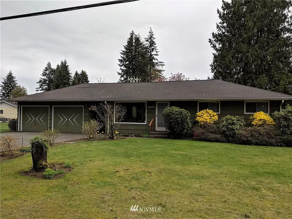 Green ranch-style house with a brown roof and a grassy lawn on a cloudy day.