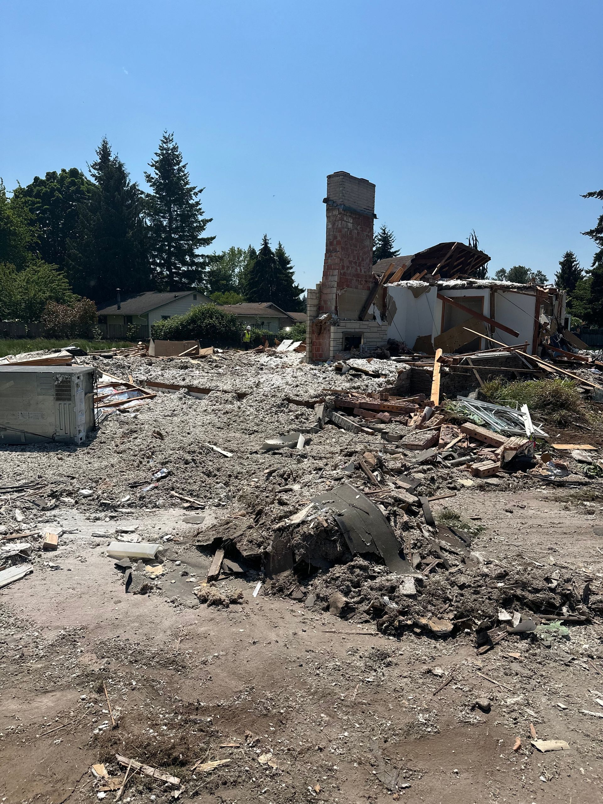 Demolished building site with rubble and a brick chimney under a clear sky.