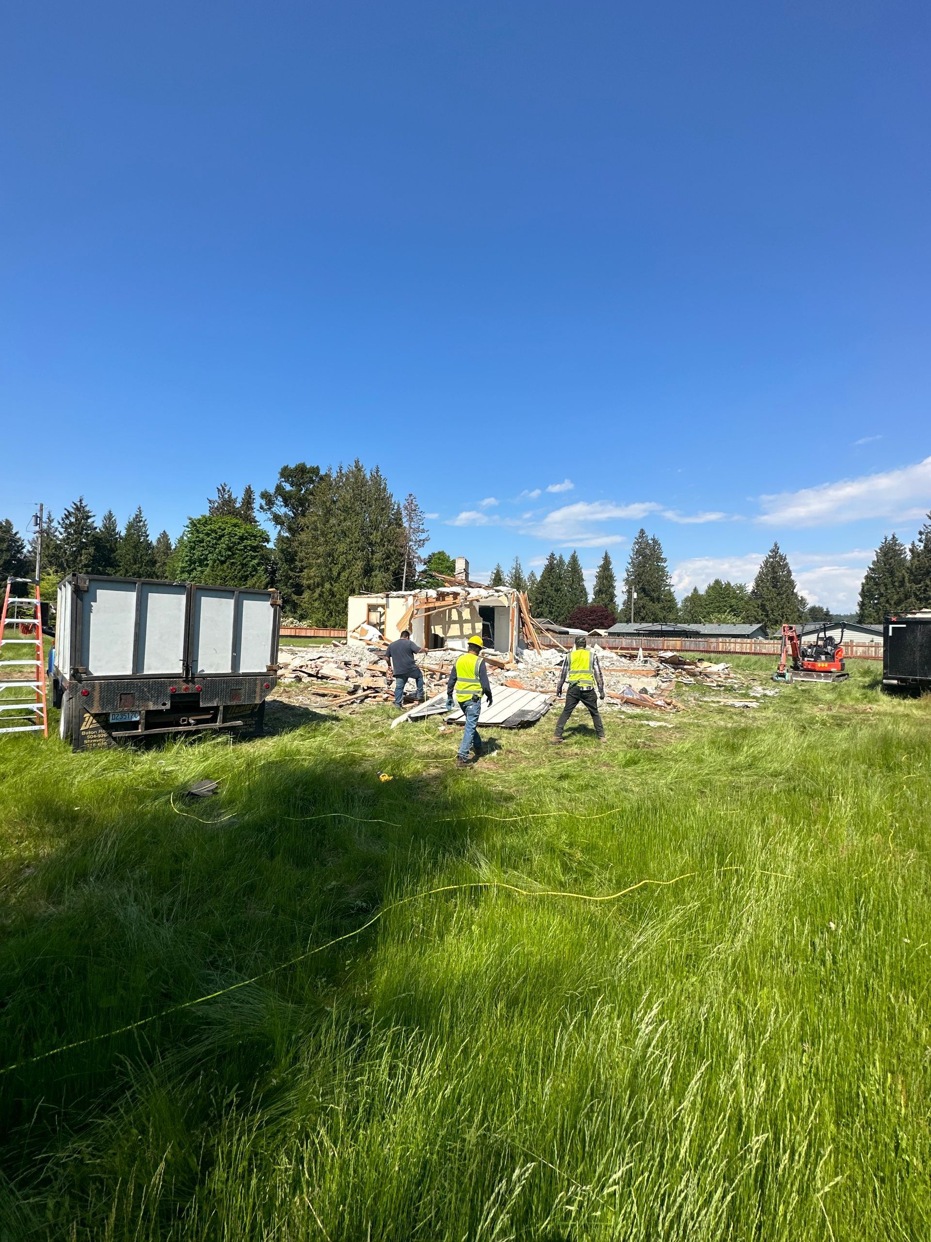 Workers in safety vests on a green field, debris of a building in the background. Dump trucks on either side.