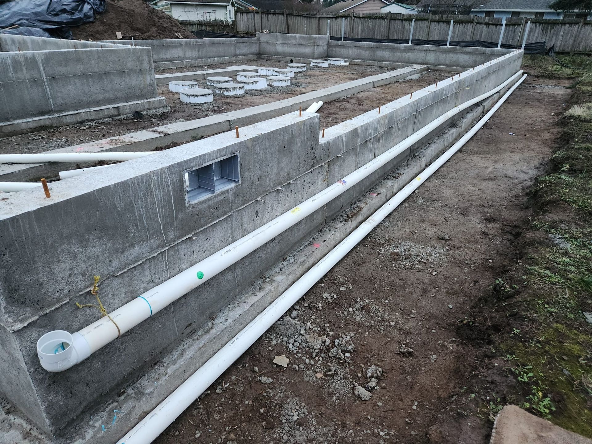 Concrete foundation with white pipes running along it, built outdoors.