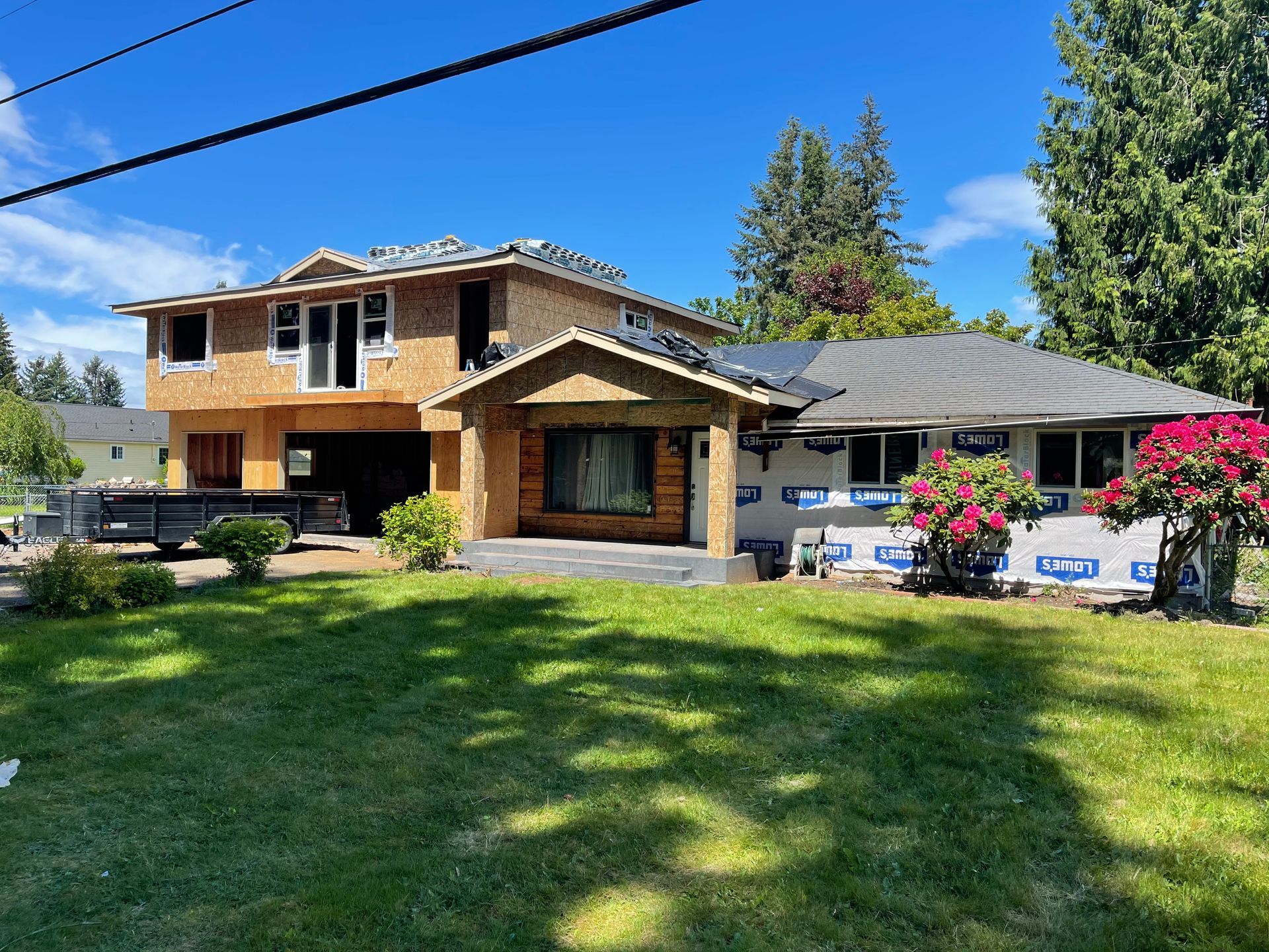 House undergoing renovation; new construction on left, existing home on right with tarpaper, blue sky.