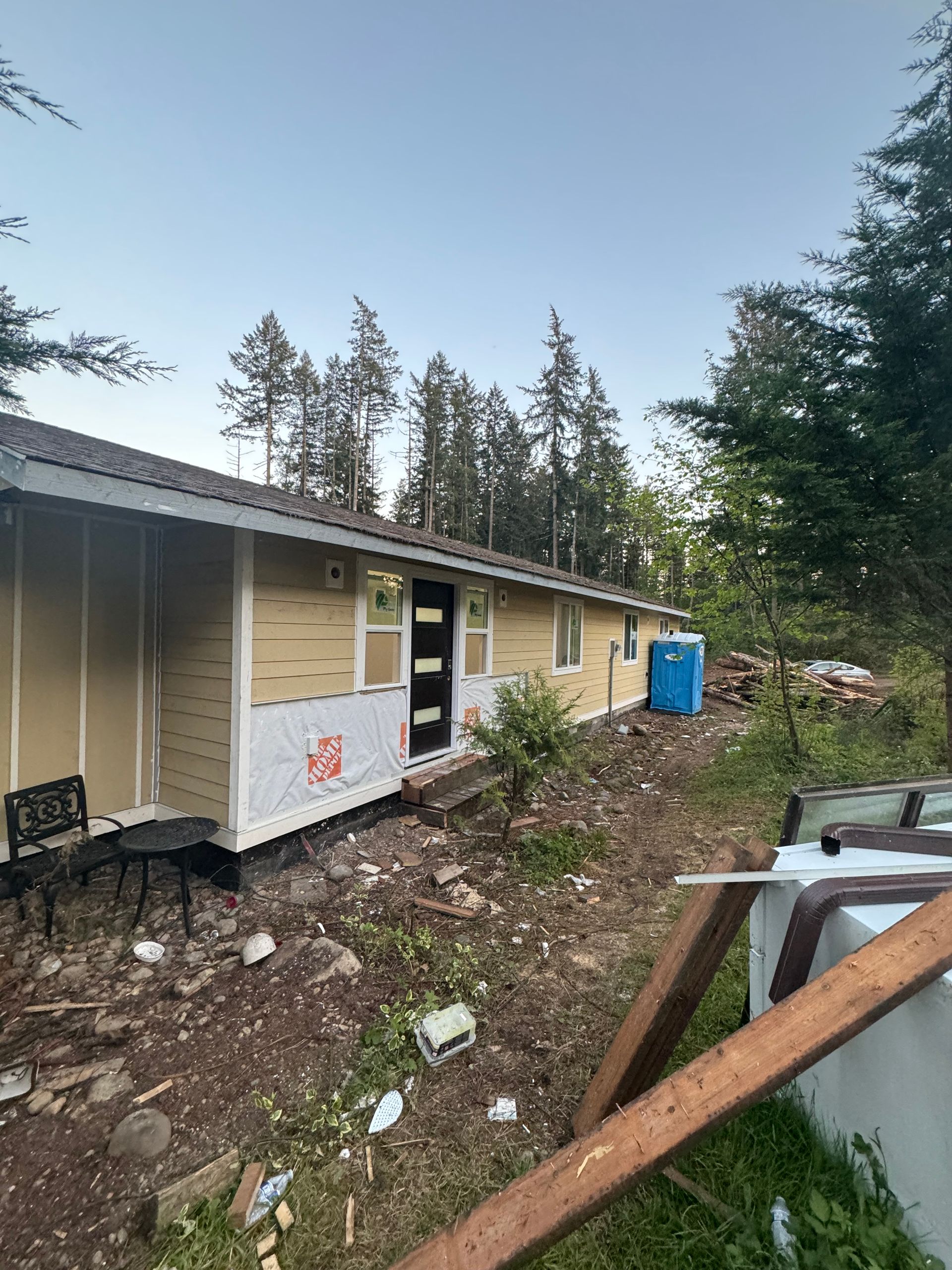 A house under construction with light yellow siding, a black front door, and a blue portable toilet.