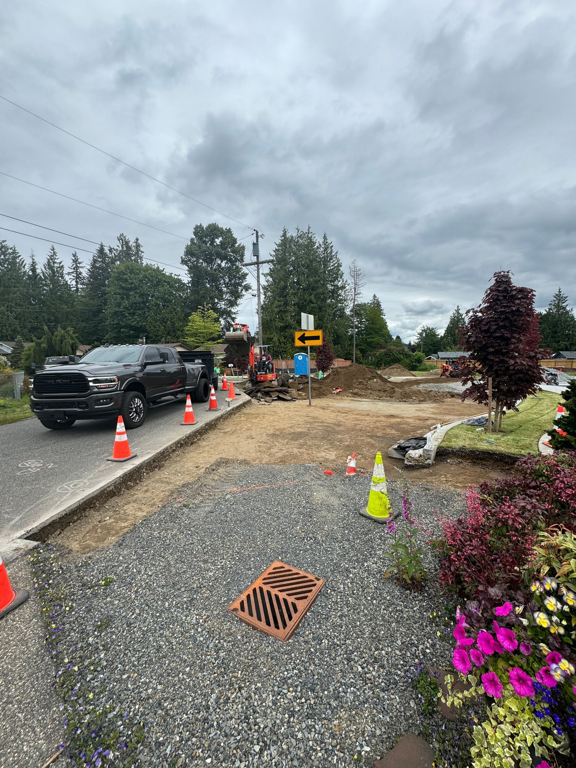 Construction site with a truck, excavator, and workers; gray gravel and dirt with orange safety cones.