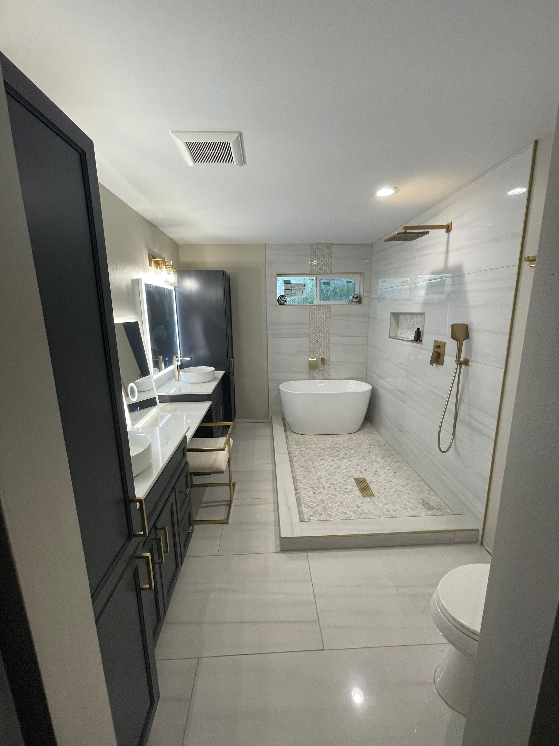 Luxurious bathroom with soaking tub, glass shower, and gold fixtures. White tile and modern design.