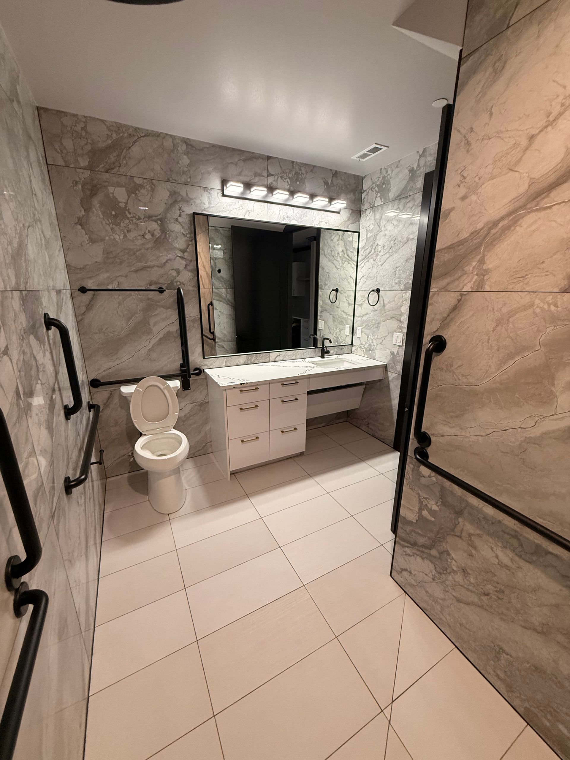 Bathroom with white tile floor, toilet, vanity, and marble-look walls.