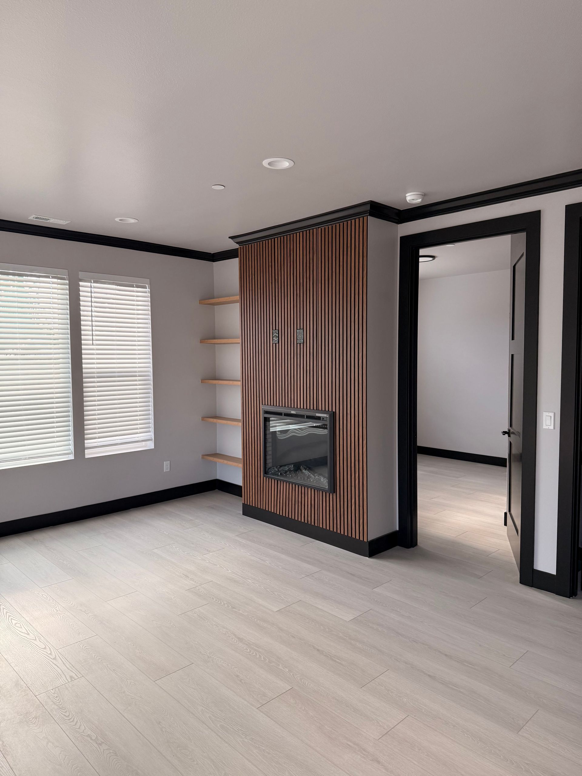 Empty room with a fireplace and shelving, accented with black trim and light wood flooring.