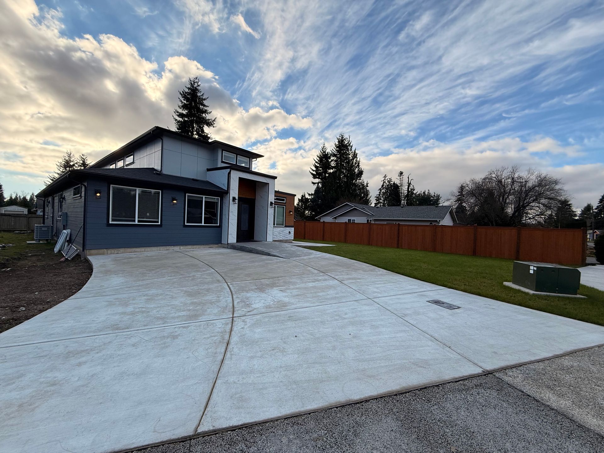 Modern two-story house with gray and white exterior, concrete driveway, and a brown fence.